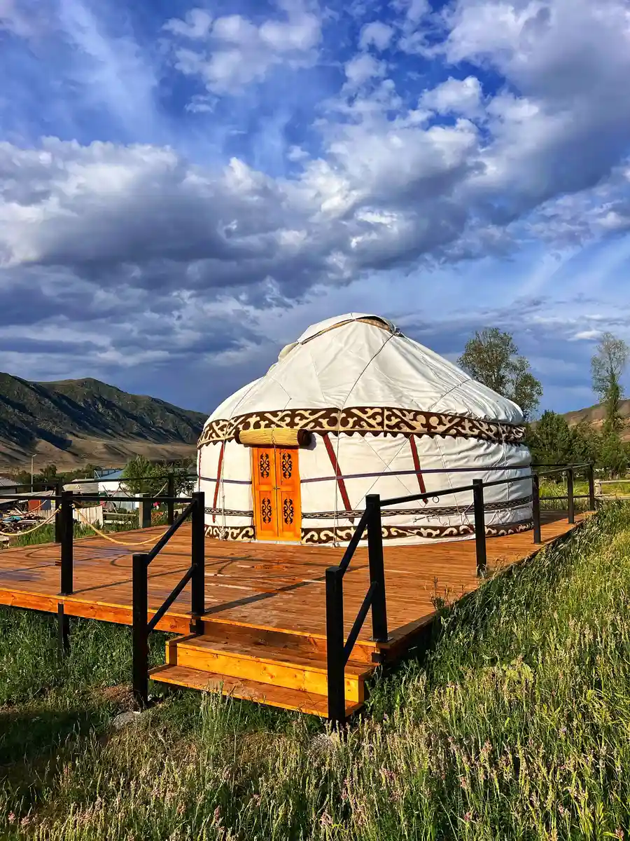 White Kazakh yurt on a wooden platform surrounded by green grass in Kolsai